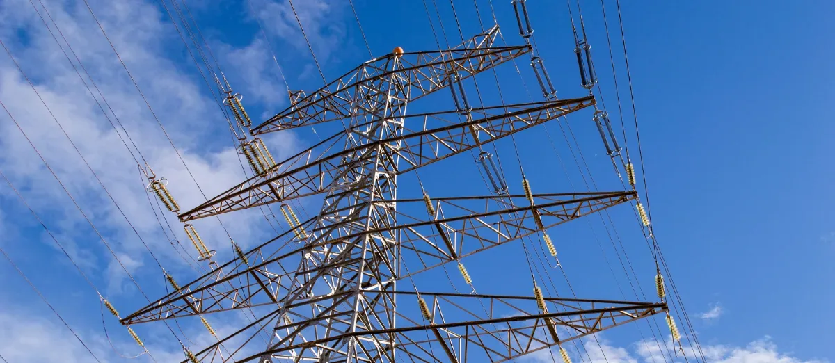 Pylône de transport d'électricité vu en contre-plongée, isolateurs et lignes haute tension se détachant sur un ciel bleu